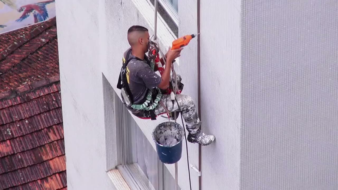 Vakman werkt aan een gevel op hoogte, hangend in een veiligheidsharnas