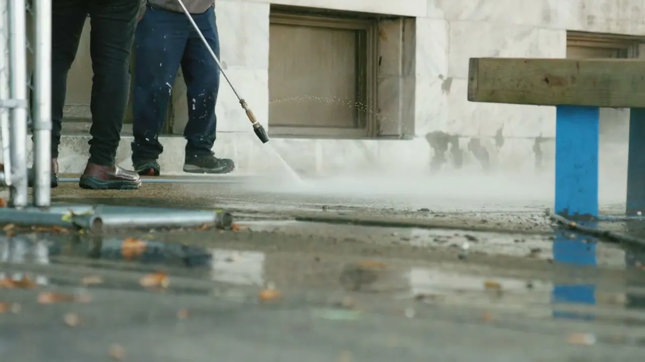 De hogedrukstraal in actie op een vuile buitenvloer langs een gevel