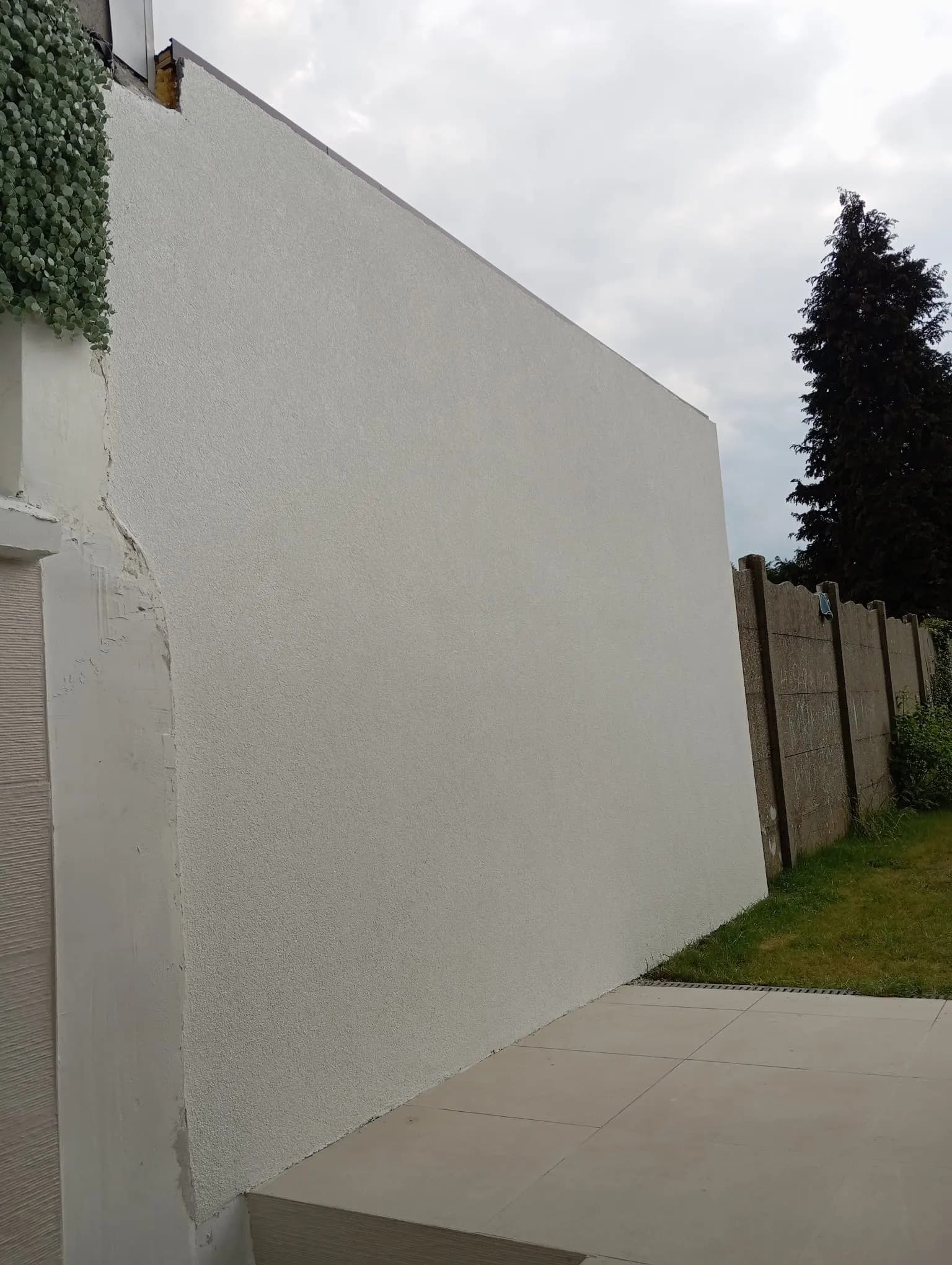 Volledig afgewerkte witte crepi-muur van een aanbouw naast een tegelterras
