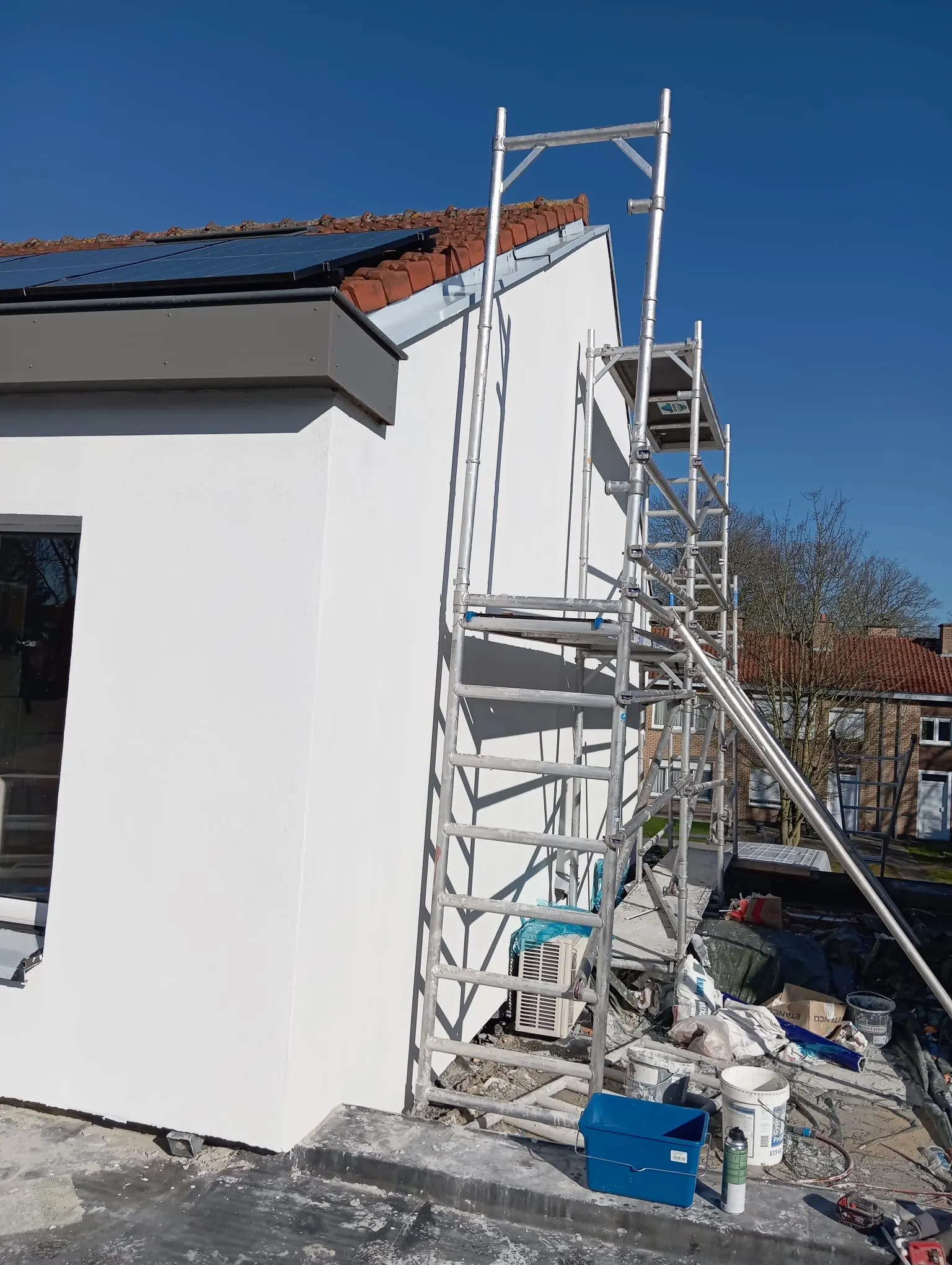 Witte afgewerkte kopgevel met rolsteiger ernaast en zonnepanelen op het pannendak