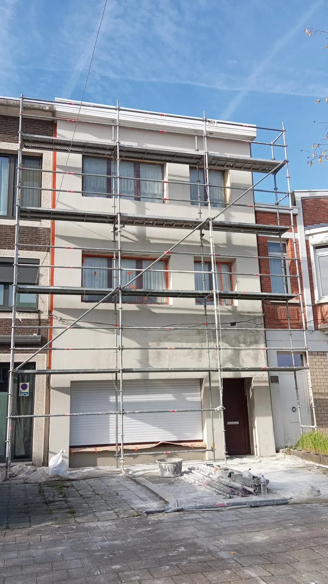 Volledige rijhuisgevel met verse pleisterlaag, in stelling en bij blauwe lucht