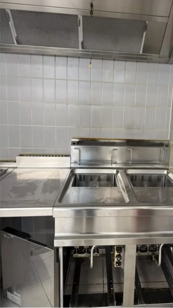 Dezelfde keuken na de reiniging: blinkende roestvrijstalen friteuse, schone afzuigfilters en vetvrije tegelwand
