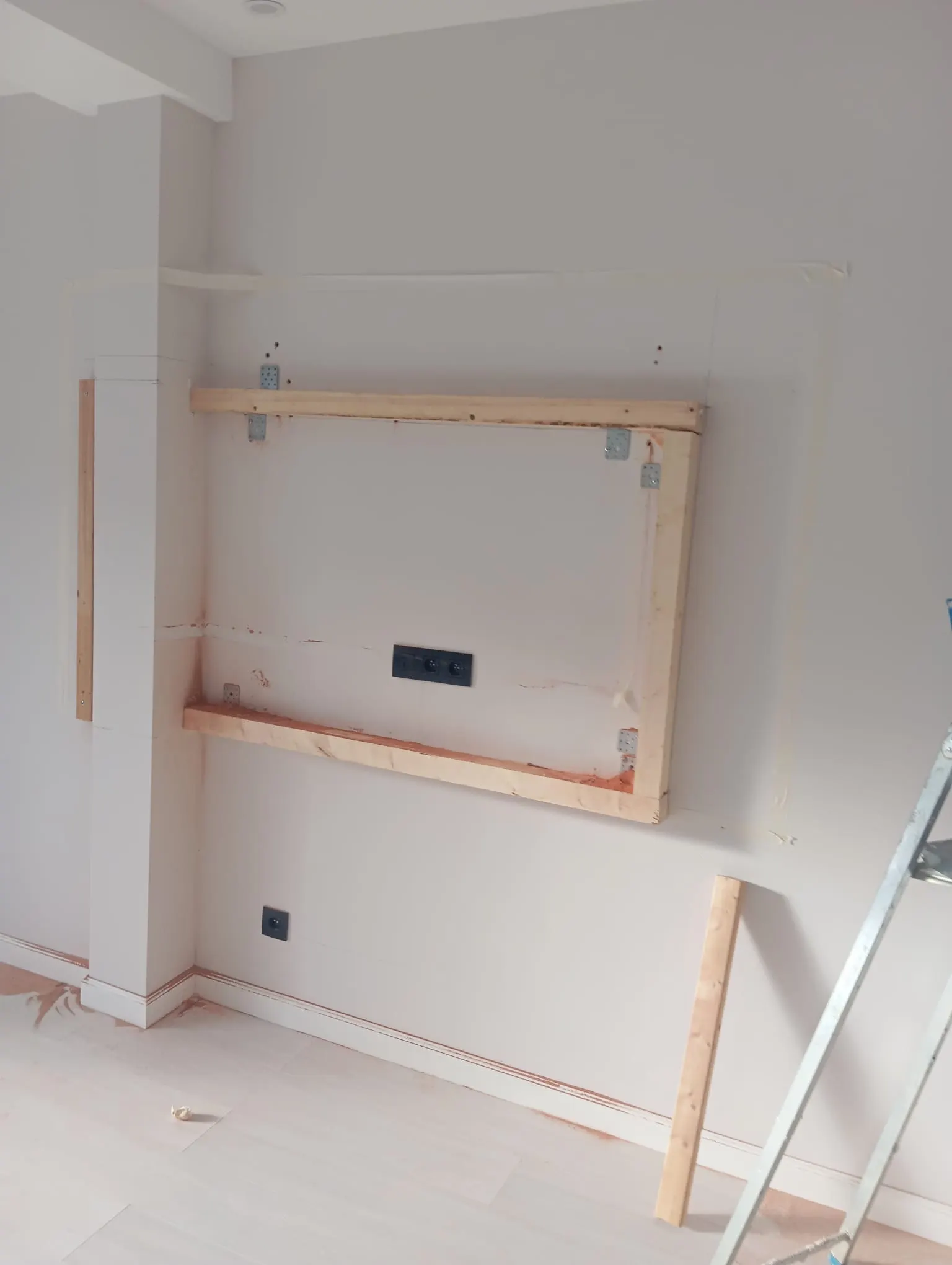 Woonkamerwand voor de afwerking: houten frame voor de tv-wand tegen een kale, afgeplakte muur