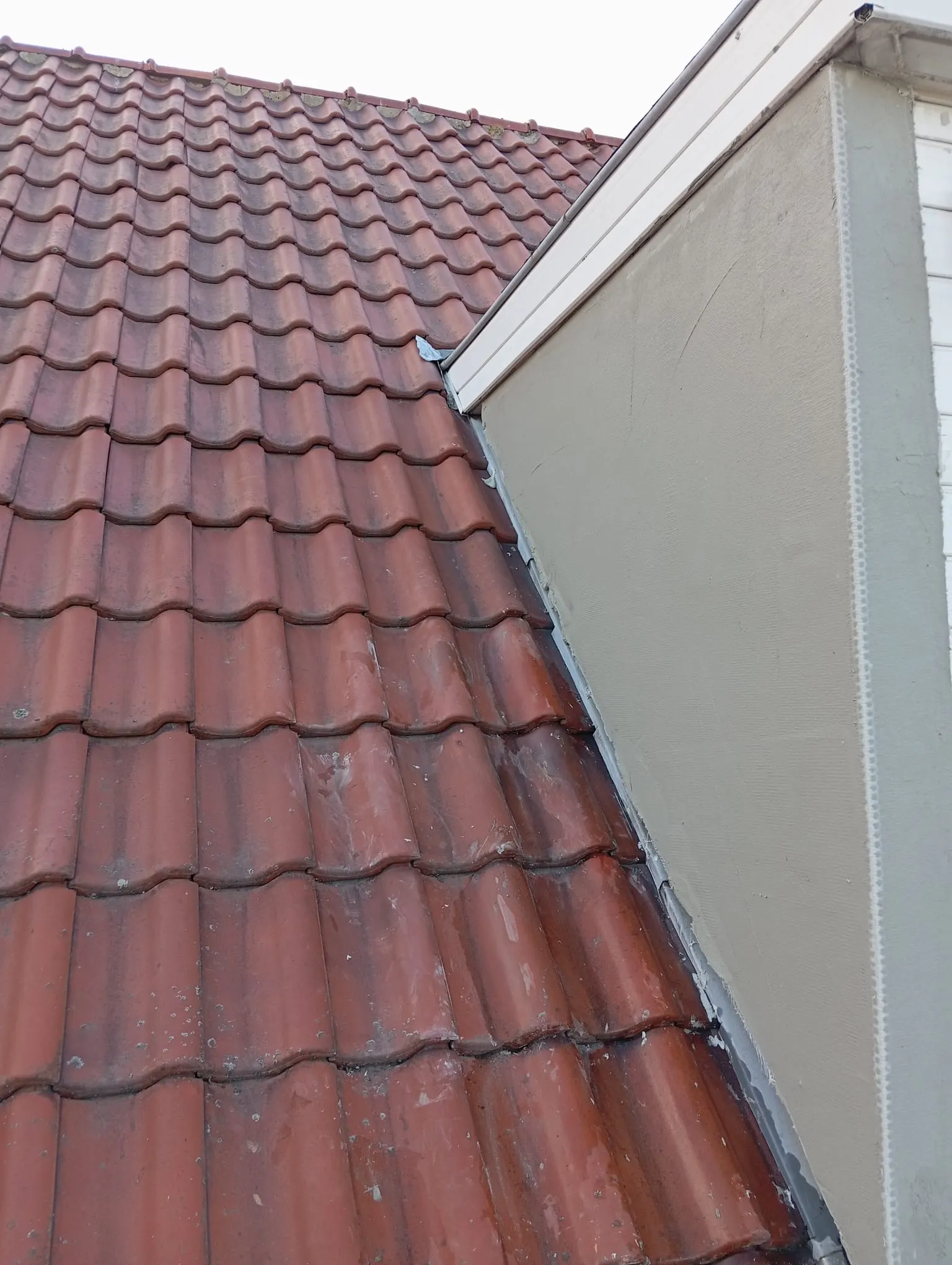 Rood pannendak dat aansluit op een gepleisterde zijgevel, met loodslabbe en dakgootrand