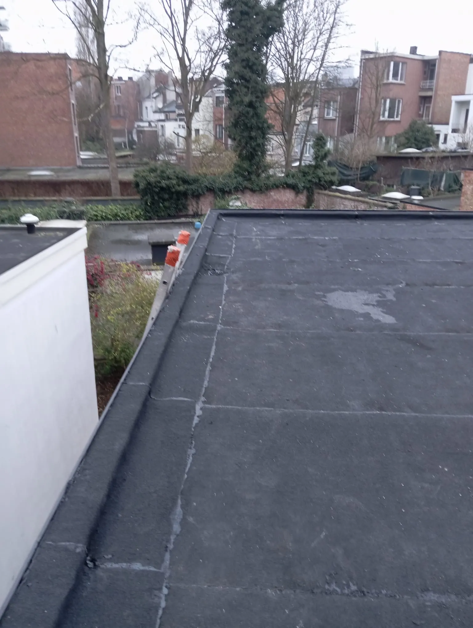 Plat dak afgewerkt met zwarte EPDM en nette dakrand, met zicht over de achtertuinen