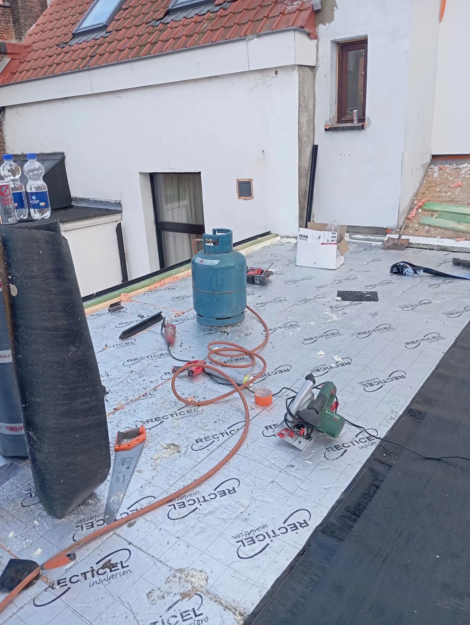 Plat dak in uitvoering: isolatieplaten geplaatst, met gasfles, brander en zaag klaar