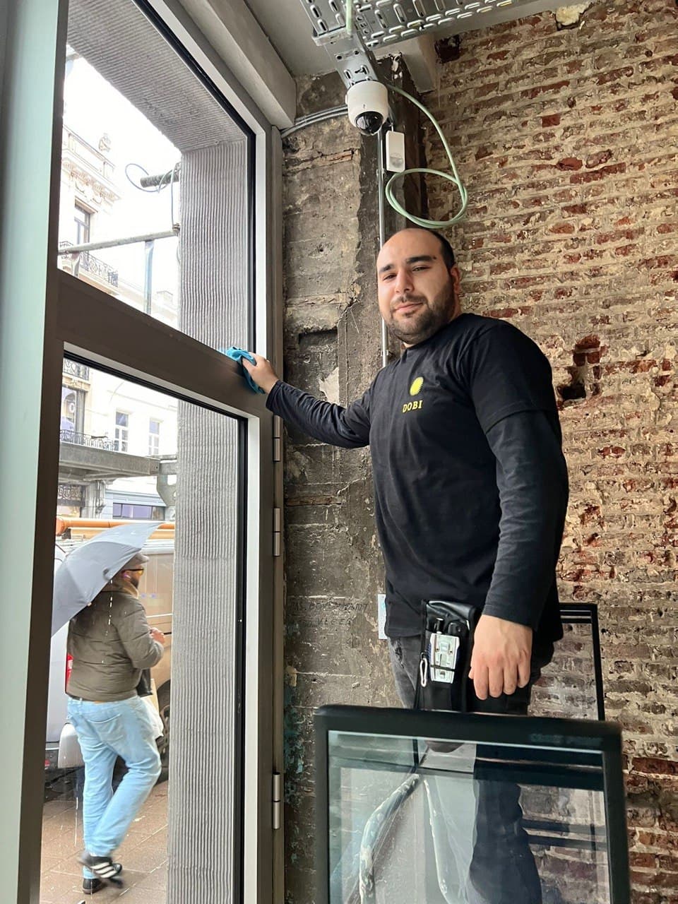 Glazenwasser Dobi Cleaning lacht bij een raam in Antwerpen